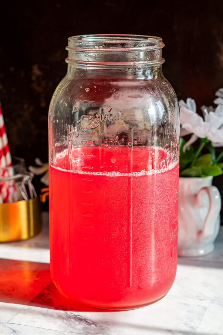 Sun shining through a bright red jar of rhubarb juice.